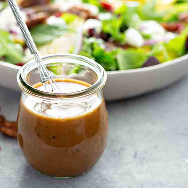 Glas Balsamicodressing vor Salat mit Löffel.