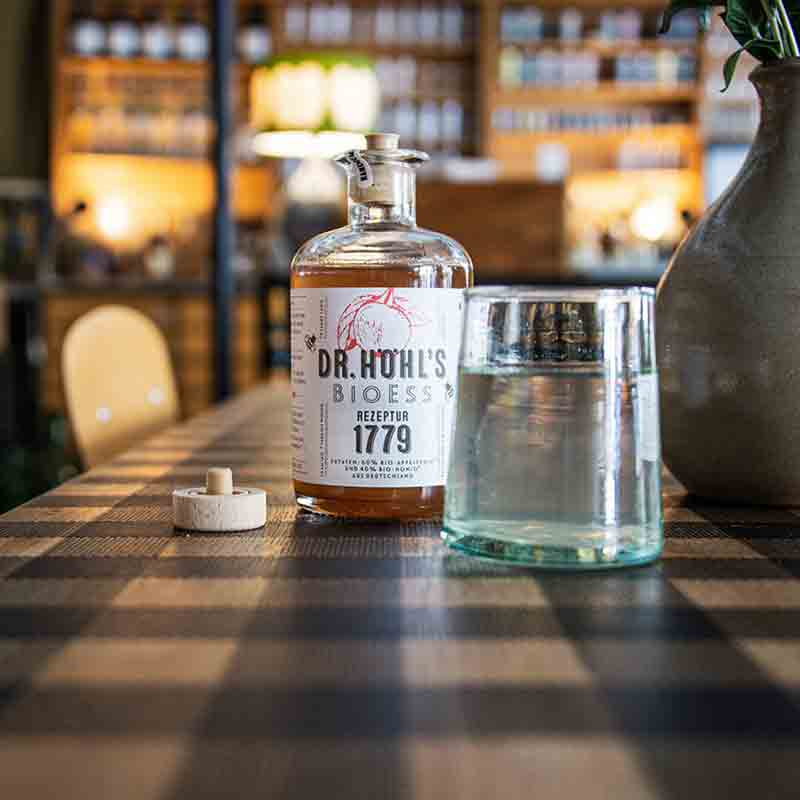 Dr. Höhl's Bioessig Flasche auf Holztisch mit Glas.
