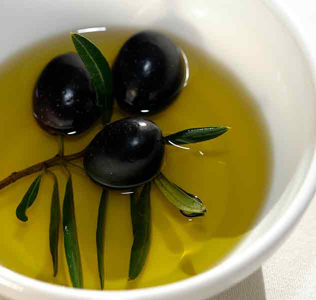 Schwarze Oliven in Schale mit Olivenöl und Zweig.