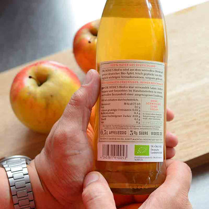 Person hält Apfelessigflasche vor Äpfeln.