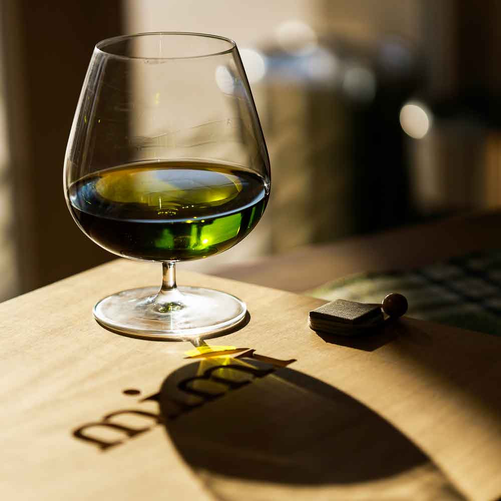 Glas mit grünem Öl gefüllt steht auch Holtztisch mit Mimi Logo