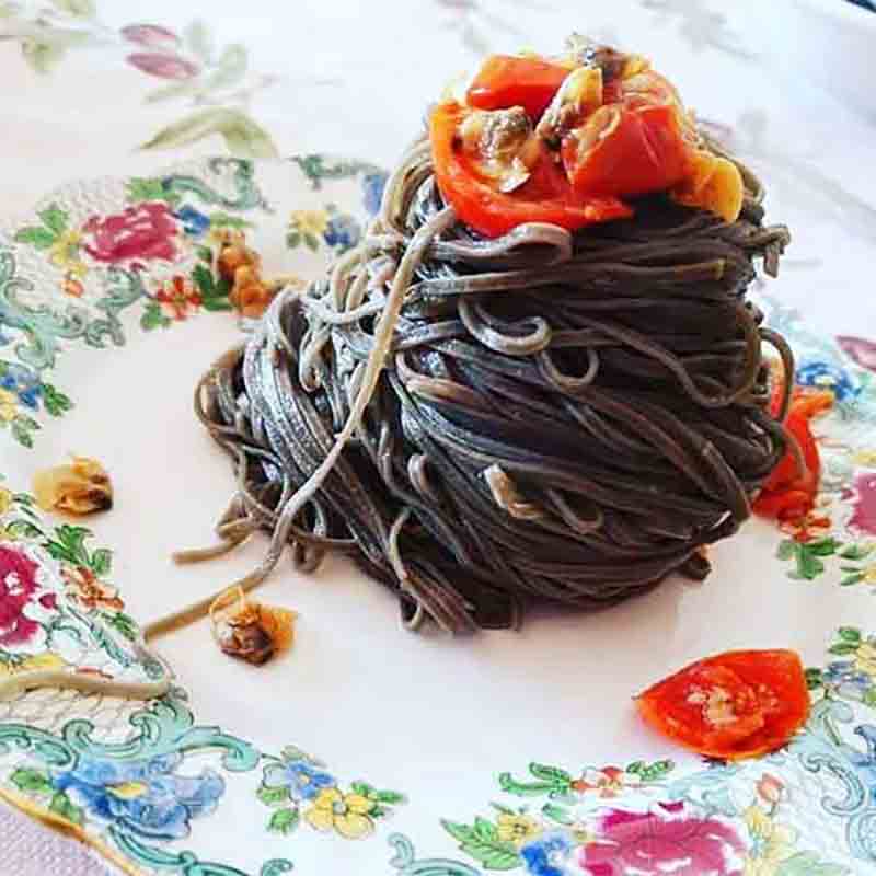 Tintenfisch-Pasta mit Tomaten auf floralem Teller angerichtet.