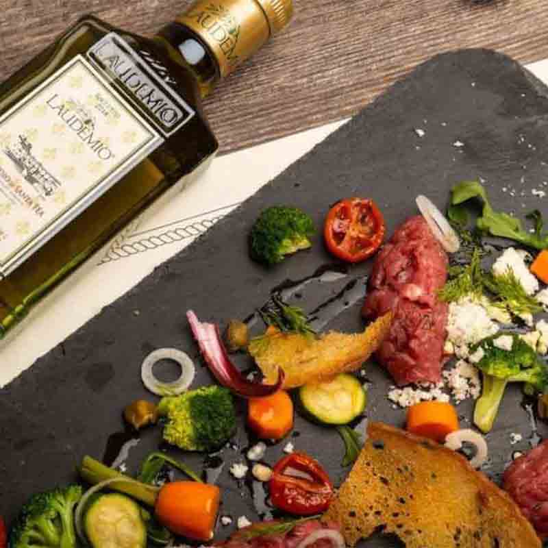 Laudemio Olivenöl neben dekorativ angerichteten Feinkostzutaten auf Schiefer.