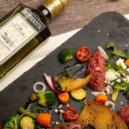 Laudemio Olivenöl neben dekorativ angerichteten Feinkostzutaten auf Schiefer.