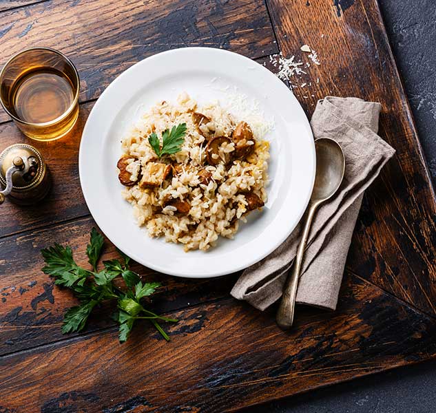 Teller mit Steinpilzrisotto, Glas Wein, Besteck, Petersilie.