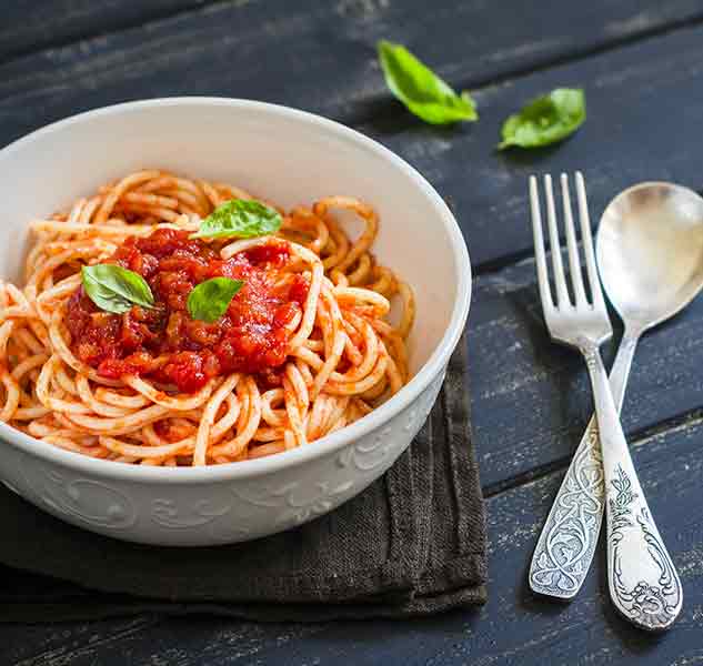 Spaghetti mit Tomatensauce und Basilikum auf dunklem Tisch.