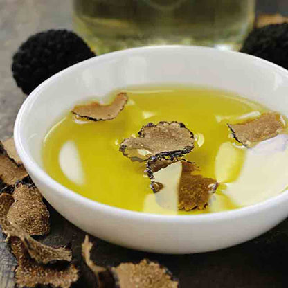 Schale mit Olivenöl und Trüffelscheiben, schwarze Trüffel daneben.