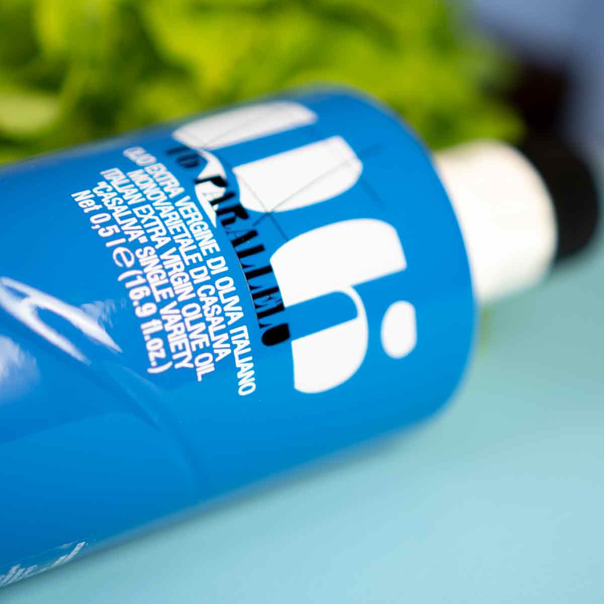 Olivenölflasche Agraria Riva Garda auf blauem Hintergrund.