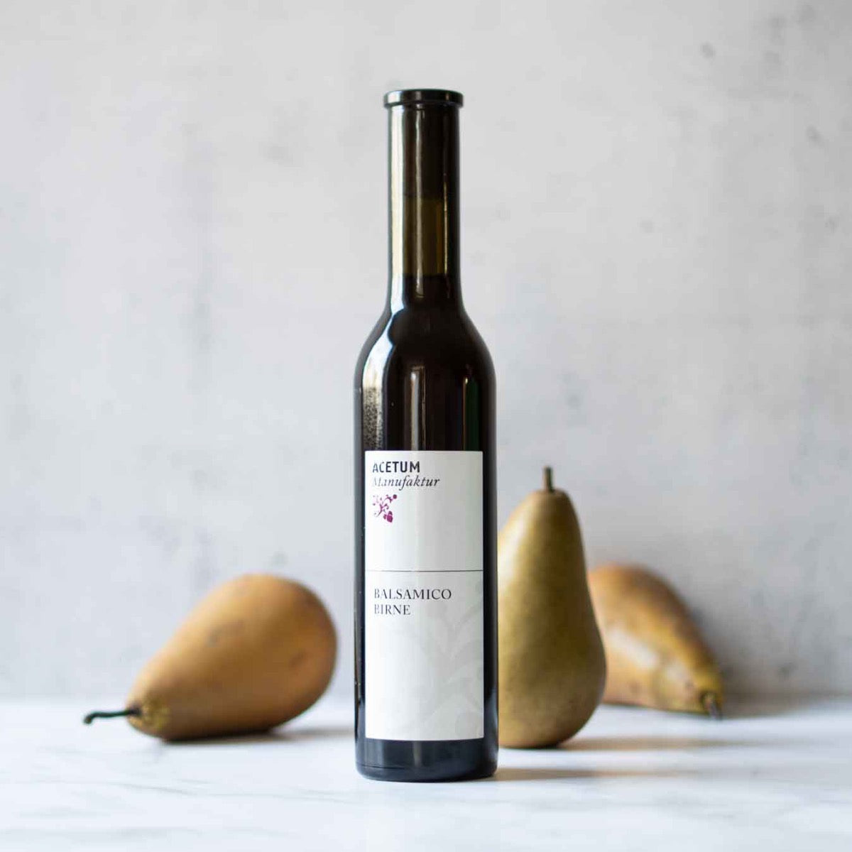 Flasche Acetum Birnenbalsamico vor zwei Birnen.