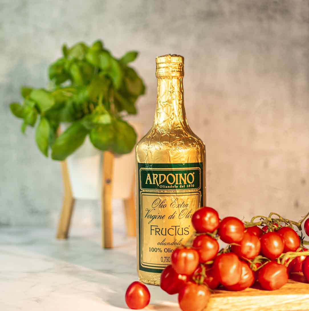 Olivenölflasche Ardoino Fructus, Basilikum, Tomaten auf Tisch.