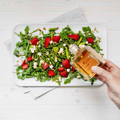 Hand hält Bellei Essig über Salat mit Erdbeeren.