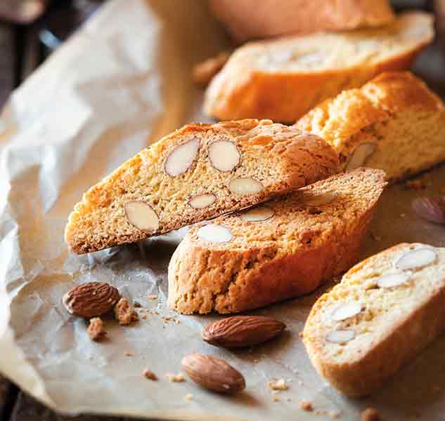 Cantuccini mit Mandeln auf Backpapier, einige ganze Mandeln.