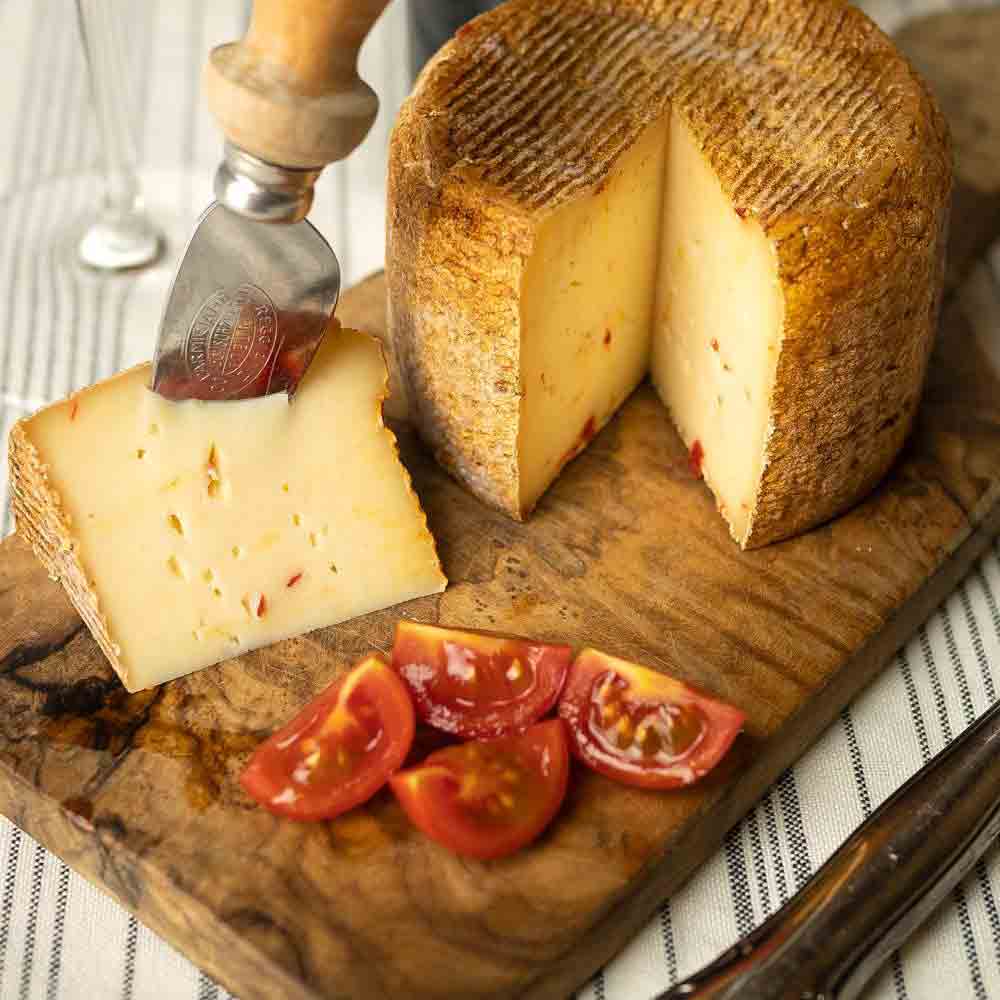 Käse mit Peperoncino, Tomaten, Messer auf Holzbrett.