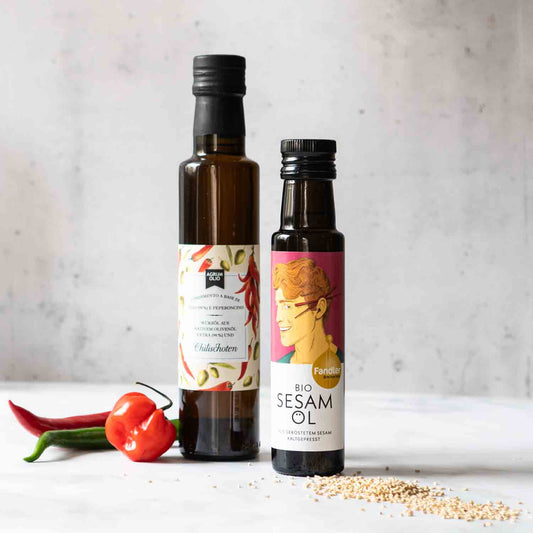 Zwei Flaschen Öl, Chilis, Sesam auf hellem Hintergrund.