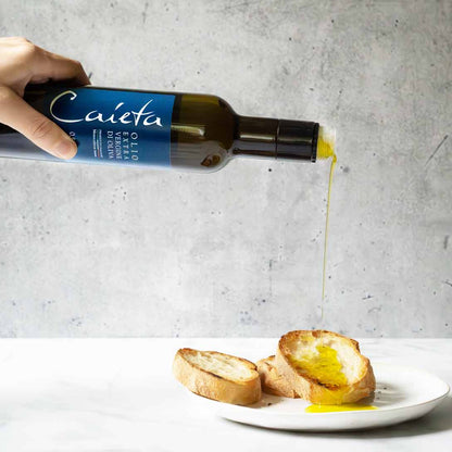 Hand gießt Caieta Olivenöl auf Brot auf Teller.