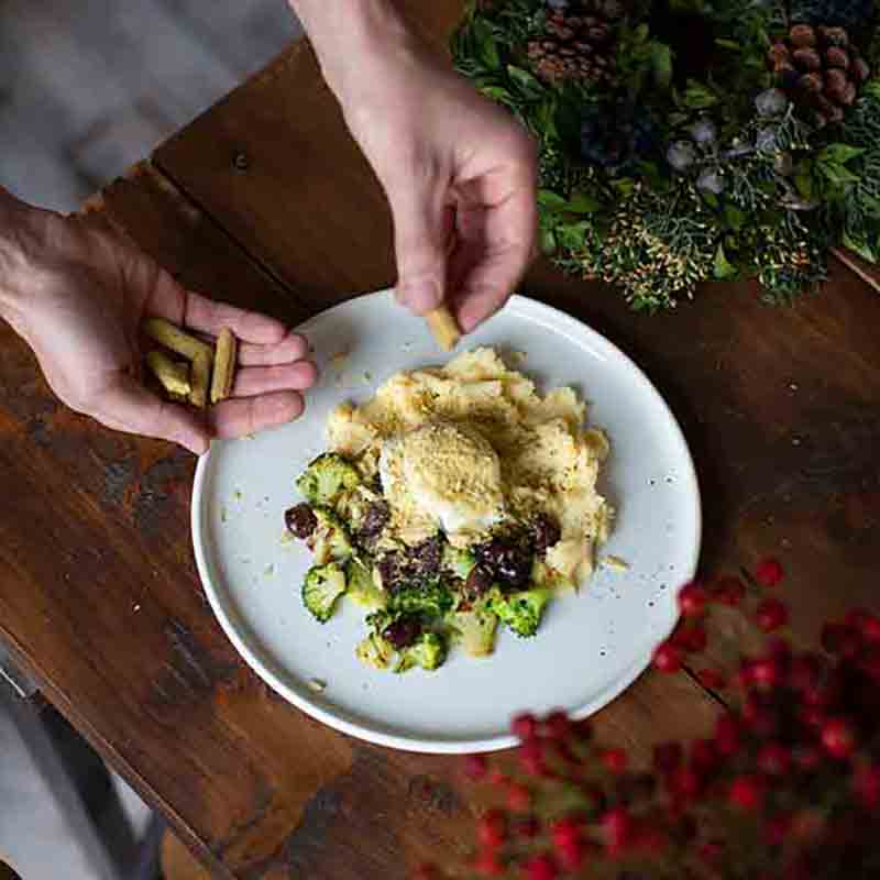 Person richtet Teller mit Pasta und Gemüse an.