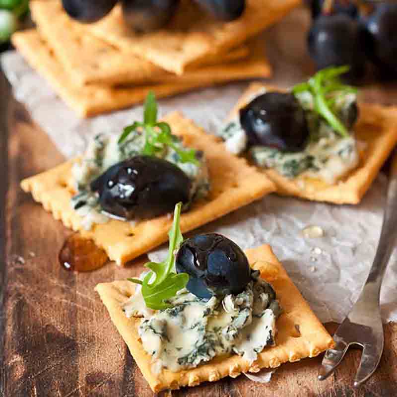 Cracker mit Blauschimmelkäse, Trauben und Rucola auf Holzbrett.