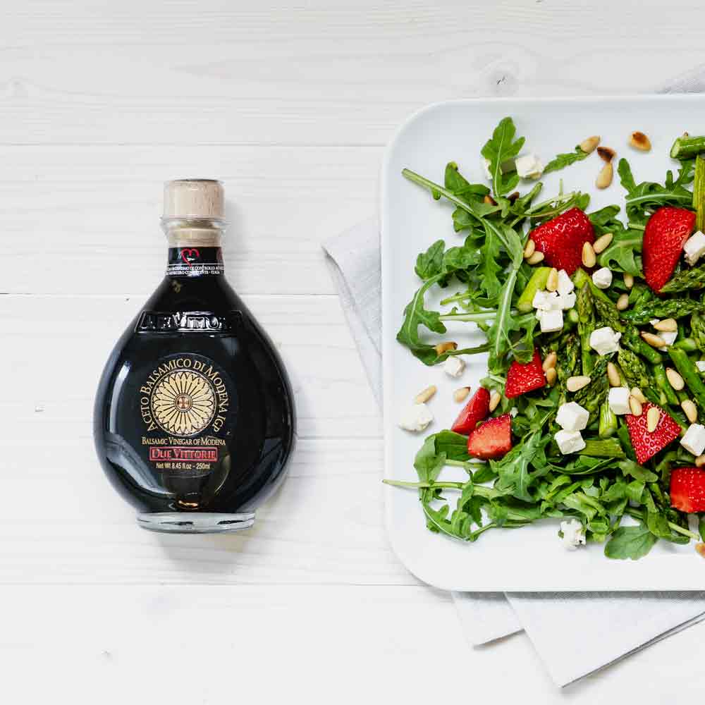 Flasche Due Vittorie Essig neben Salat auf weißem Tisch.