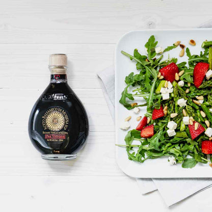 Flasche Due Vittorie Essig neben Salat auf weißem Tisch.