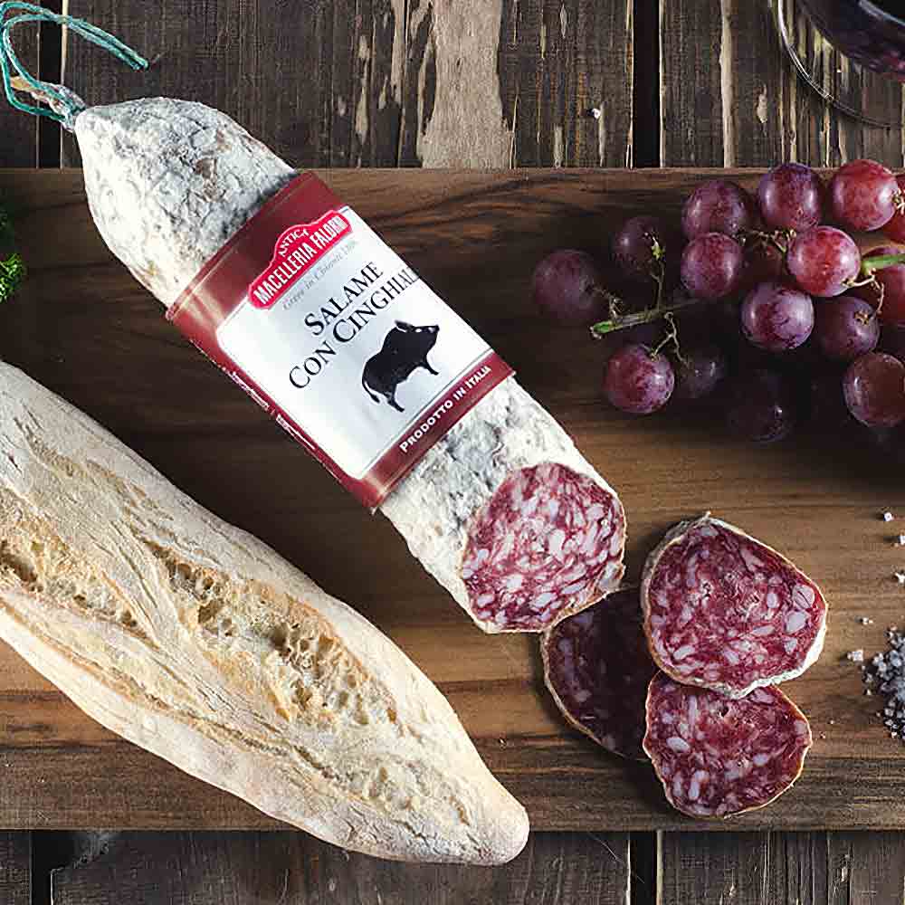 Salami, Baguette, Trauben und Salz auf Holztisch arrangiert.