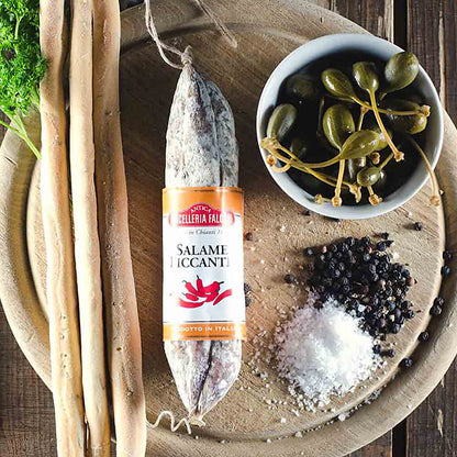 Salami, Grissini, Kapern, Salz, Pfeffer auf Holzbrett arrangiert.