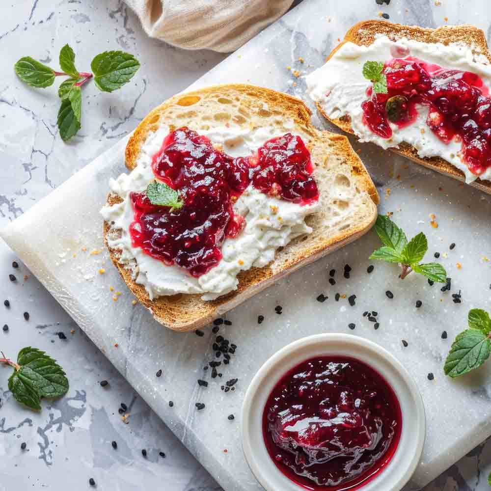 Brot mit Frischkäse und roter Konfitüre auf Marmorplatte.