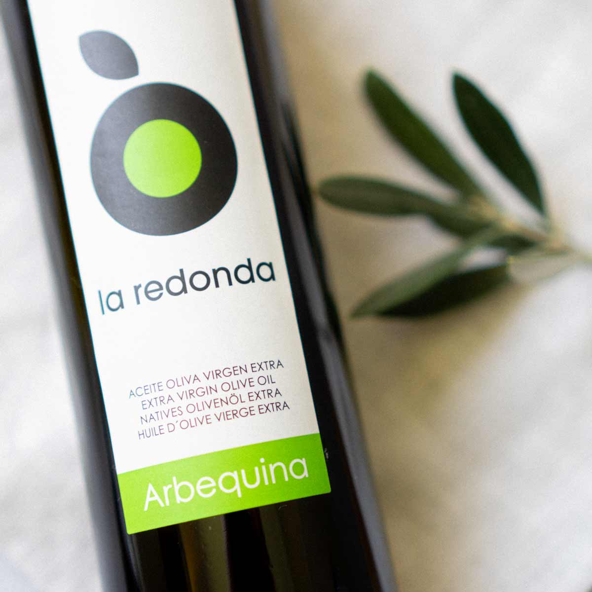 Olivenölflasche "la redonda" mit Olivenzweig daneben.