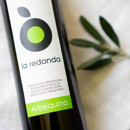 Olivenölflasche "la redonda" mit Olivenzweig daneben.