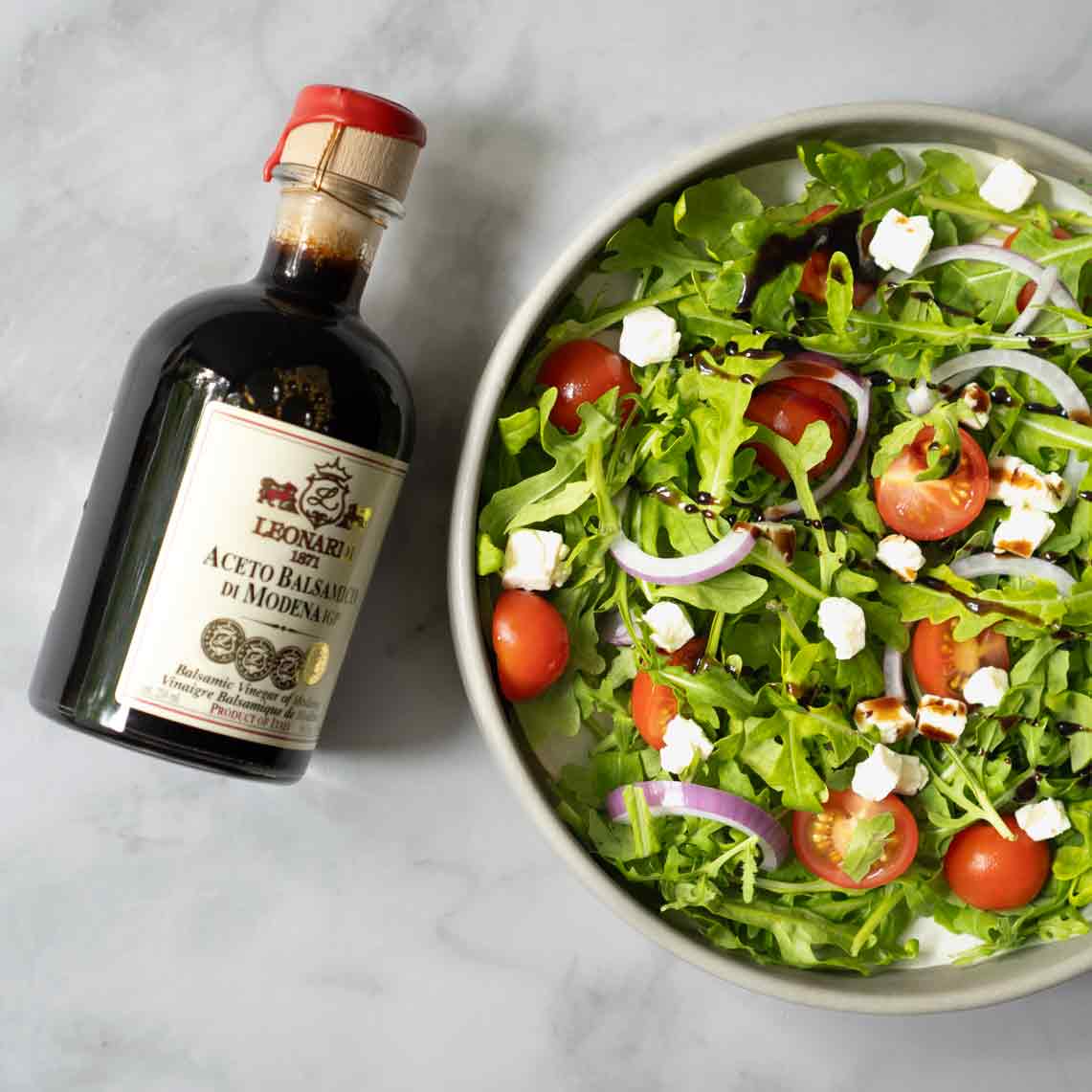 Leonardi Balsamico neben Salatschüssel mit Tomaten und Zwiebeln.