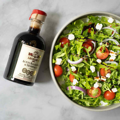 Leonardi Balsamico neben Salatschüssel mit Tomaten und Zwiebeln.