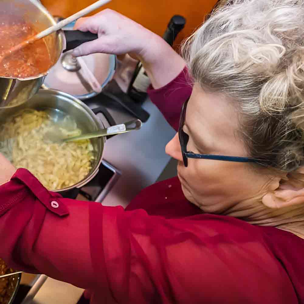 Frau kocht Pasta mit Soße.
