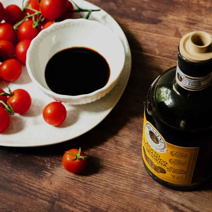 Tomaten, Schale mit Essig, Mussini-Flasche auf Holztisch.