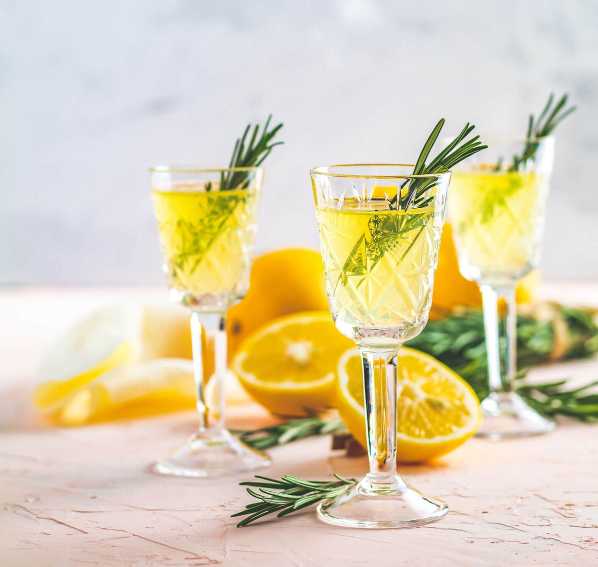 Drei Gläser Limoncello mit Rosmarin und Zitronen.
