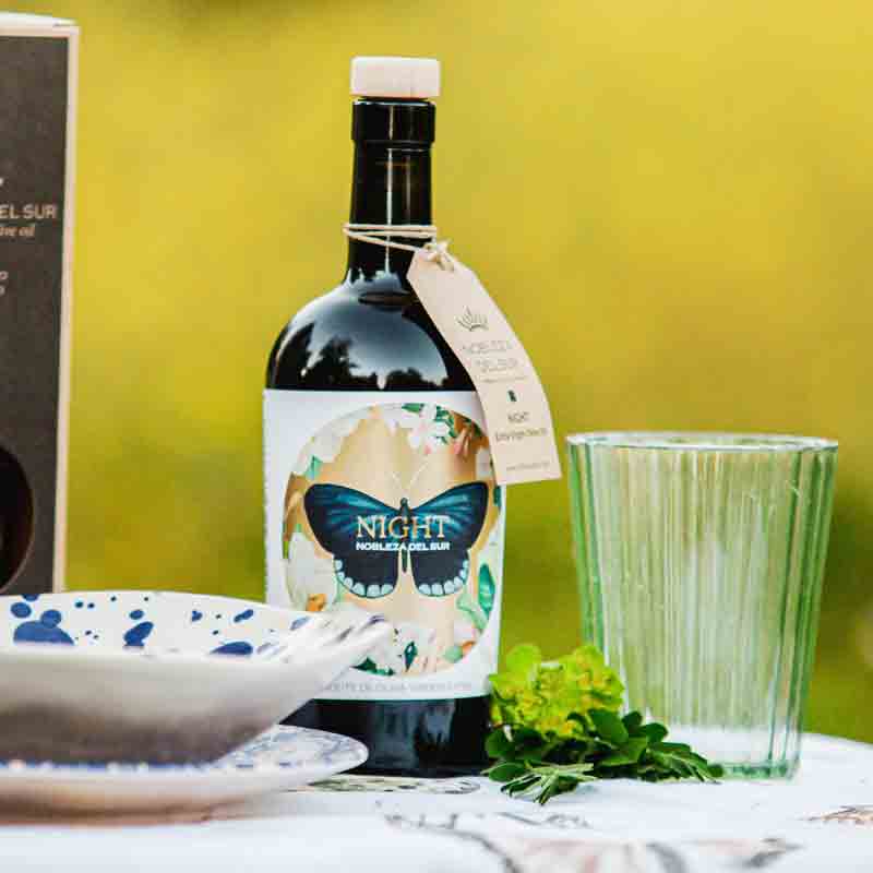 Olivenölflasche "Nobleza del Sur Night" mit Geschirr und Glas.
