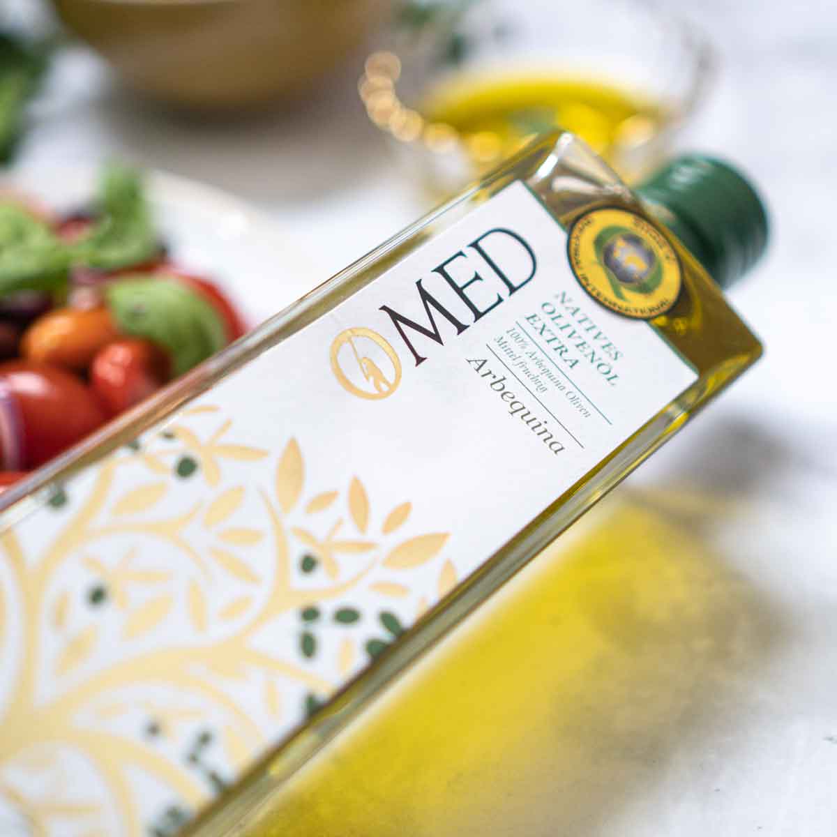 O-MED Olivenölflasche liegend, im Hintergrund Tomaten und Basilikum.
