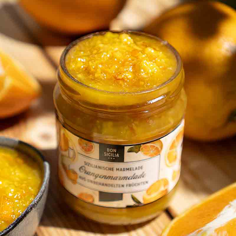 Bon Sicilia Orangenmarmelade im Glas mit Orangen im Hintergrund.
