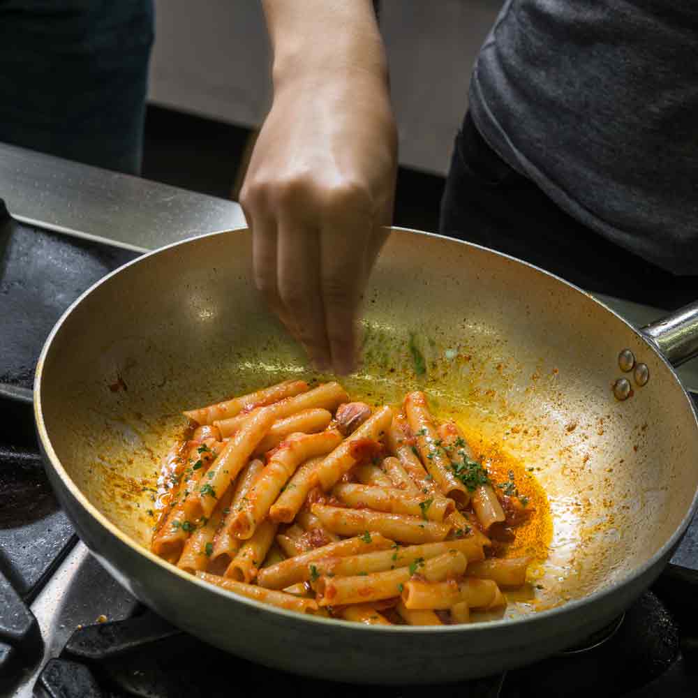 Person kocht Ziti-Pasta mit Colatura in Pfanne.