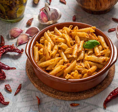 Penne mit Chilipesto in Schale, umgeben von Knoblauch.
