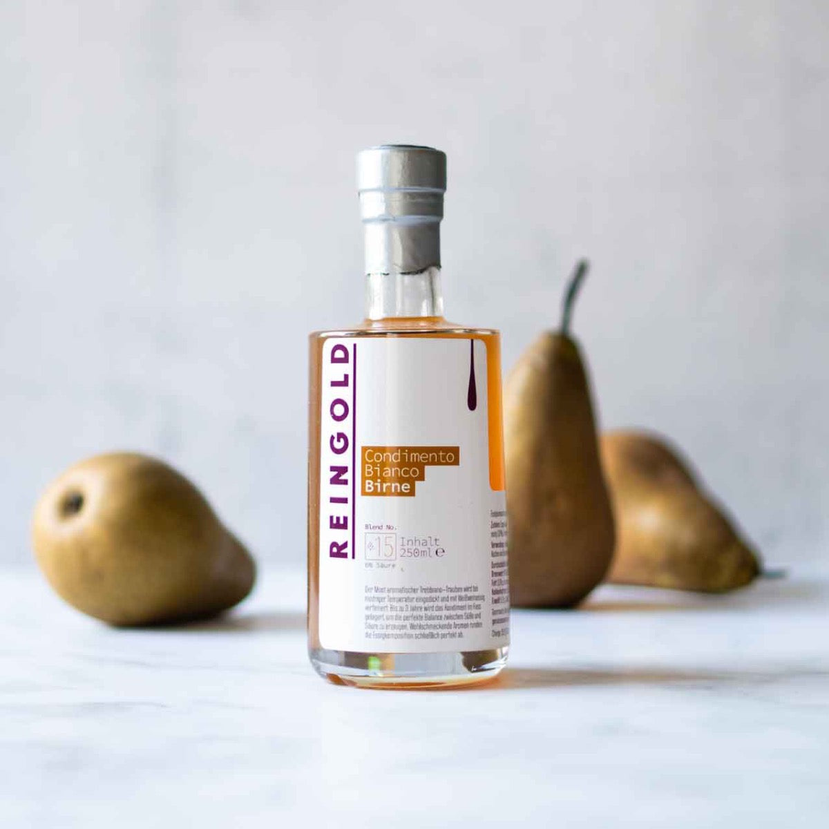 Reingold Birnenbalsamflasche vor Birnen auf hellem Hintergrund.