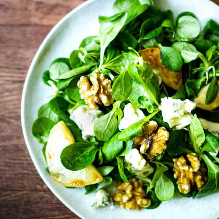 Salat mit Birnen, Walnüssen und Dressing auf Teller.