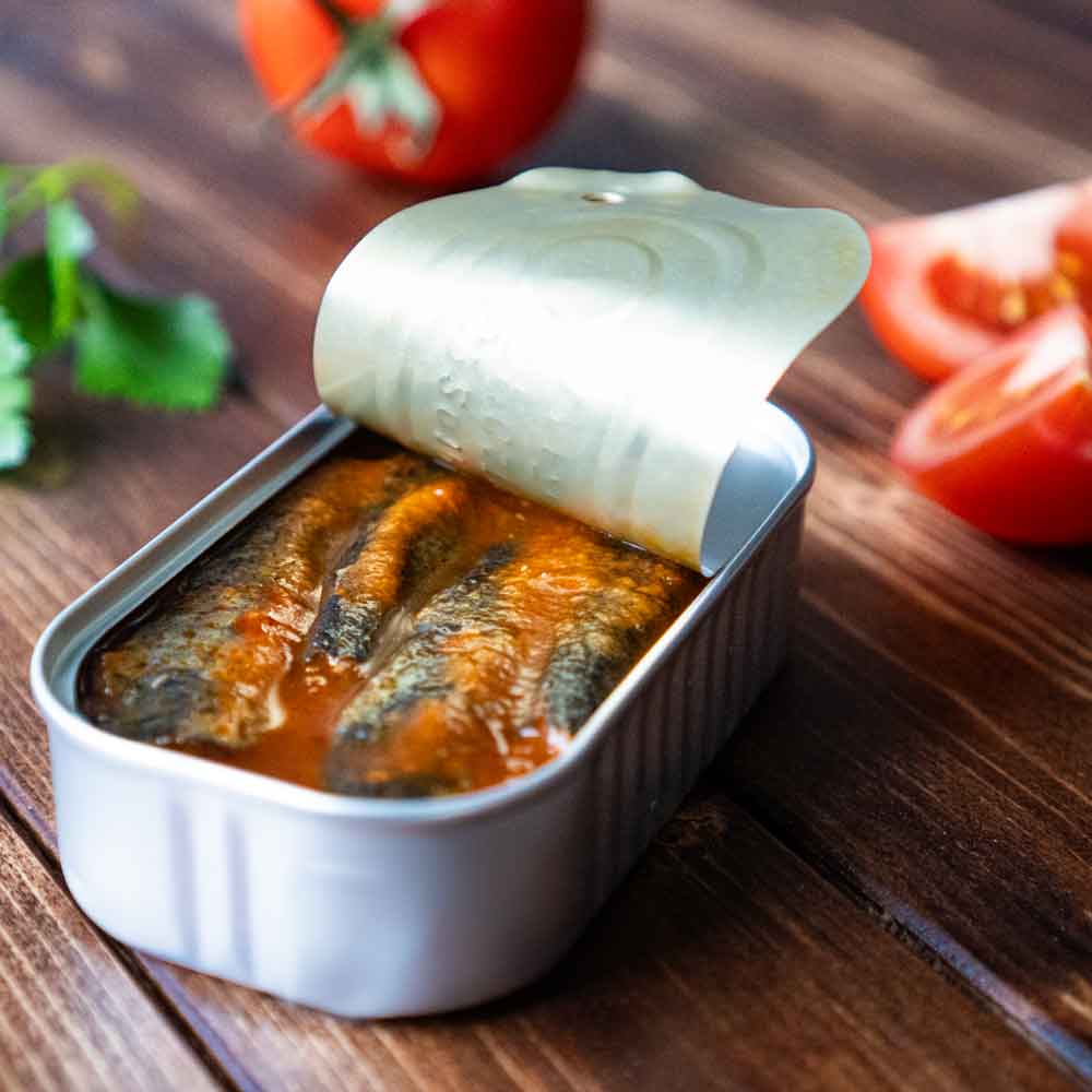 Geöffnete Sardinenbüchse mit Tomaten auf Holztisch.