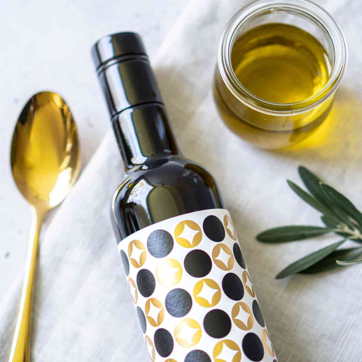 Tenute Librandi Olivenölflasche, Löffel, Glas, Olivenzweig, Tischdecke.