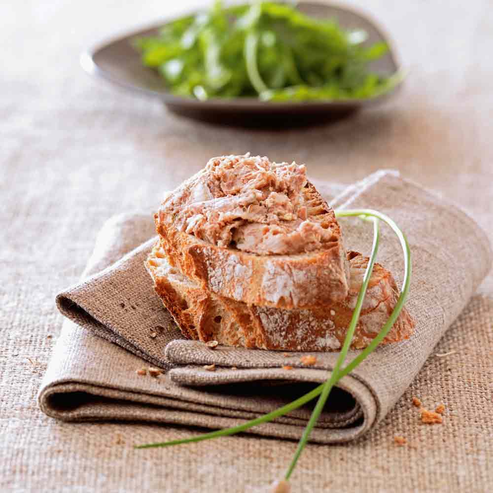 Brot mit Aufstrich auf Serviette, Salat im Hintergrund.