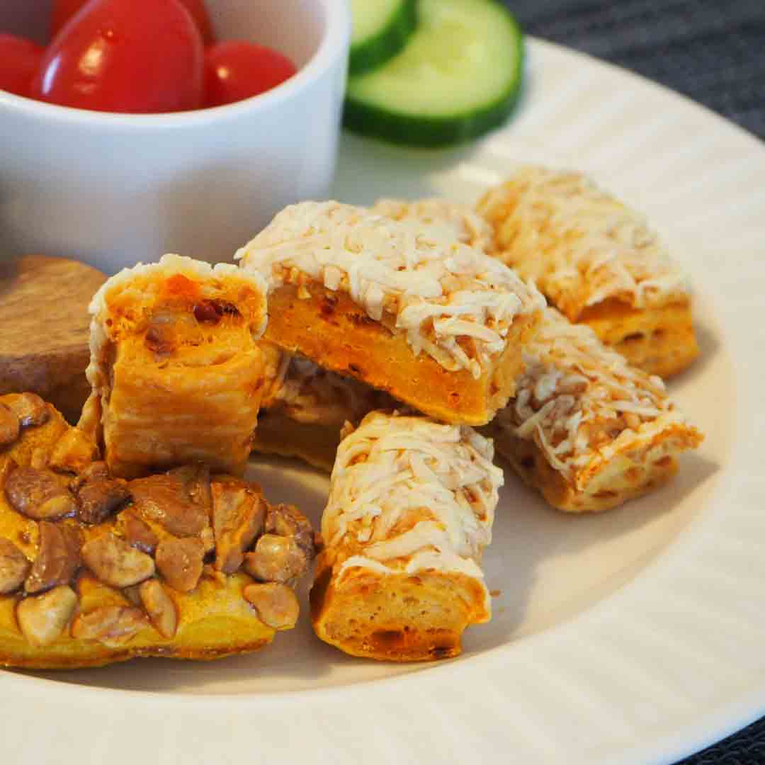 Käsegebäck, Nussriegel, Tomaten, Gurken auf weißem Teller.