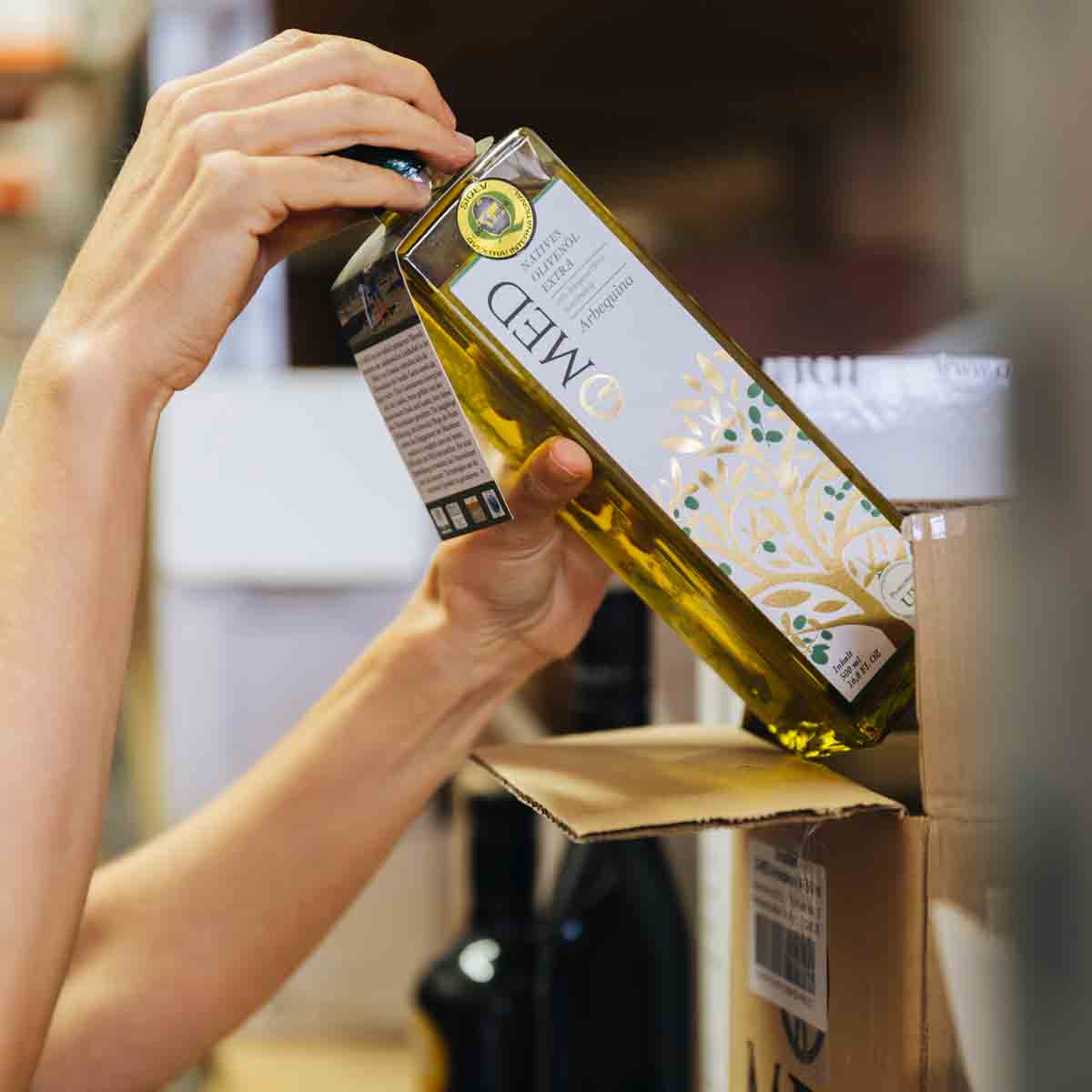 Person verpackt Olivenölflasche der Marke MED in Karton.
