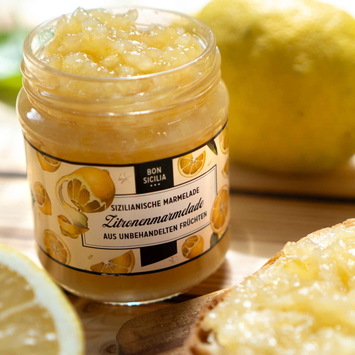 Bon Sicilia Zitronenmarmelade im Glas mit Zitronen im Hintergrund.