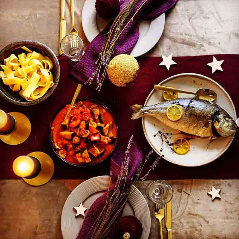 Feinkost-Tisch mit Fisch, Pasta, Gemüse, Kerzen und Dekoration.